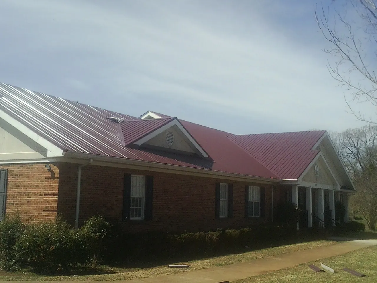 Red metal roof with gabled entries on a long brick building, from a Hail Damage Roof Repair job in Edisto Island