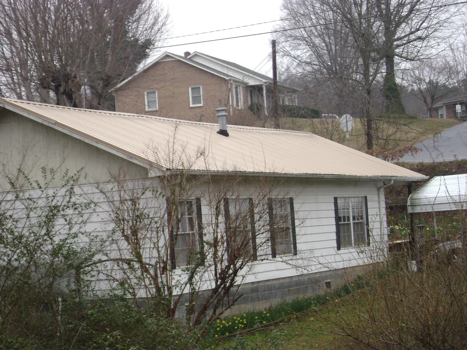 Tan metal roof on a white sided house set into a hillside — Commercial Roofing by Roofing Brothers in Edisto Island
